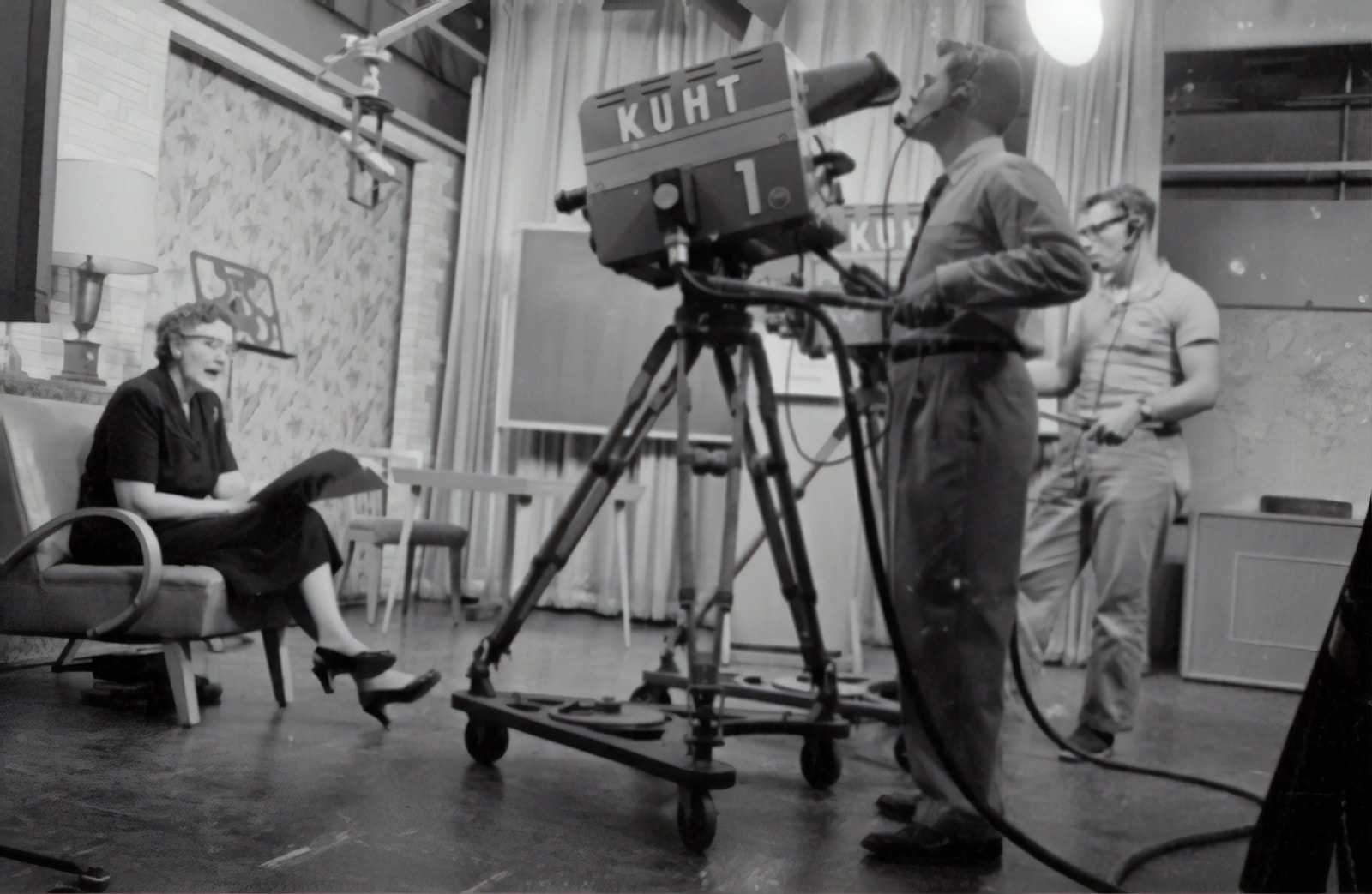 grayscale photography of man standing near studio camera and woman sitting while holding book